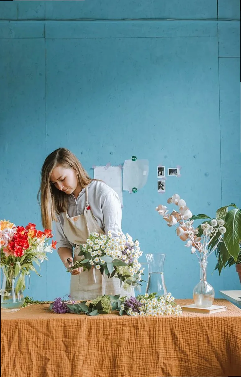 A florist arranges colorful flowers on a table in a bright indoor workshop.